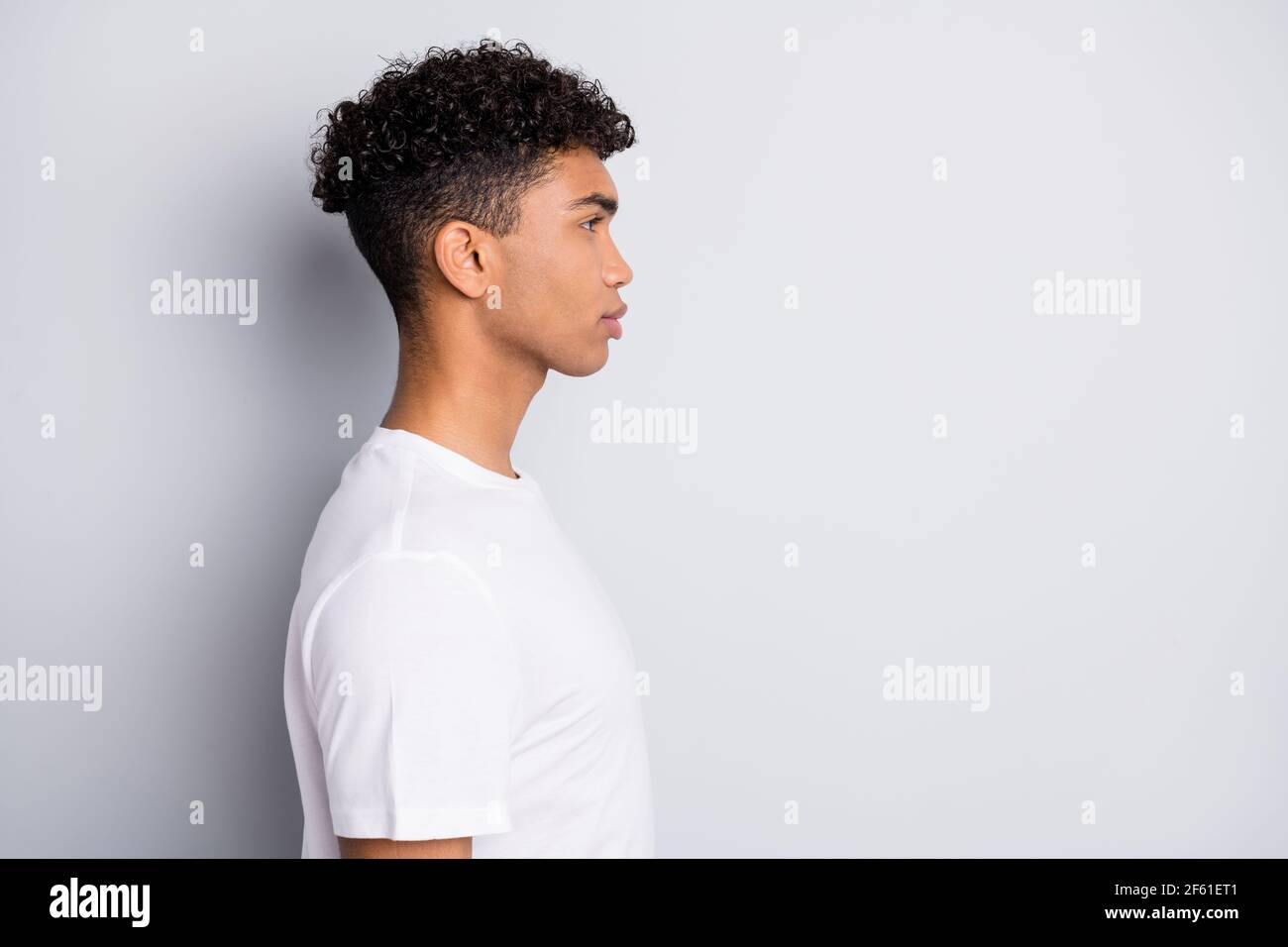 Perfil retrato de morena optimista chico rizado parece espacio vacío use  una camiseta blanca aislada sobre fondo gris Fotografía de stock - Alamy