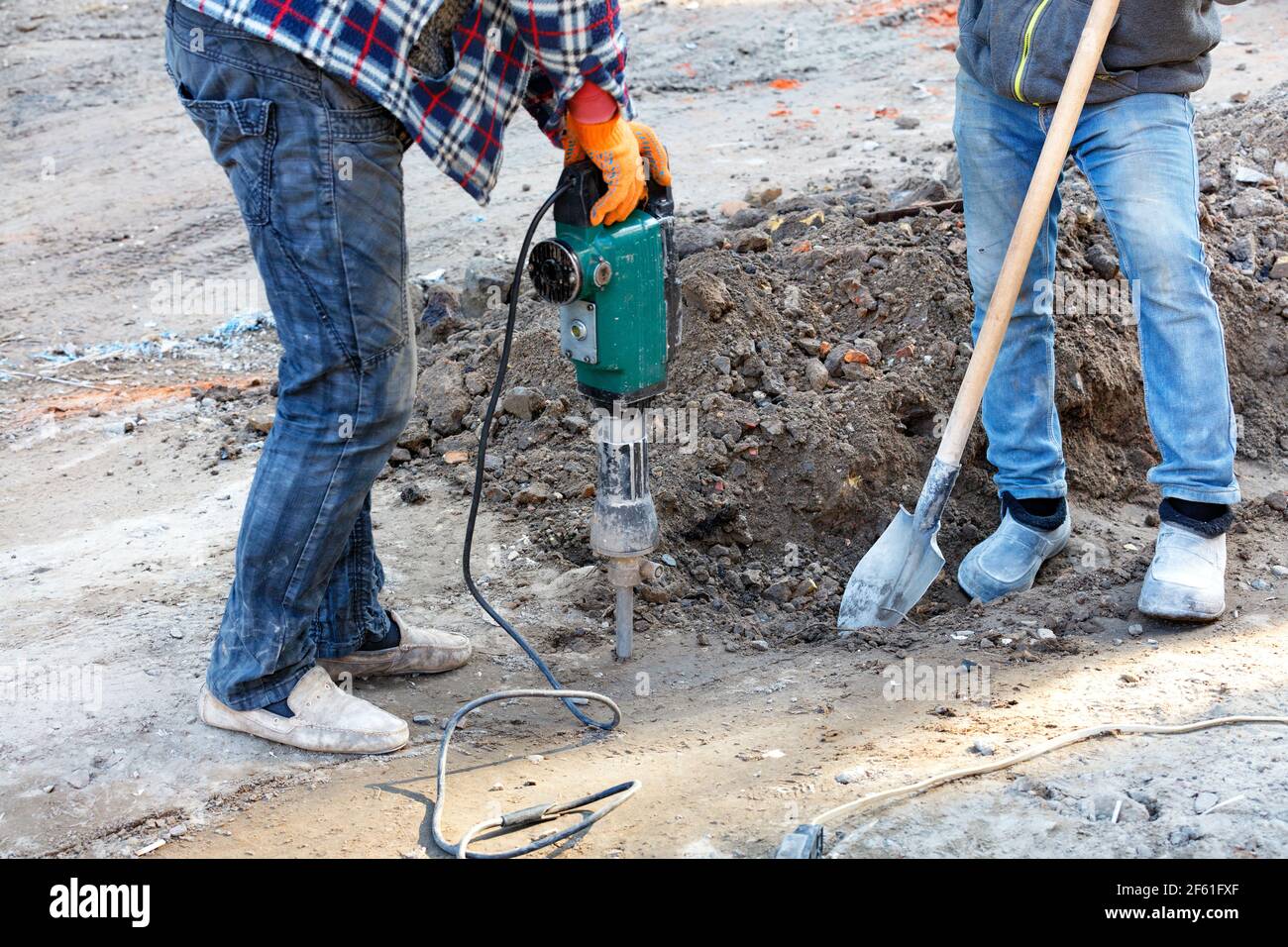 Los constructores en un sitio de construcción están aflojando el suelo  denso con un martillo de inercia eléctrico y una pala Fotografía de stock -  Alamy