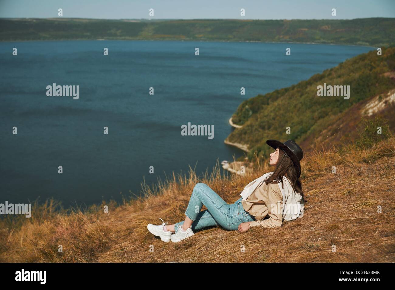 Jovencita caminadora relajándose en la cima de la montaña y disfrutando de la hermosa naturaleza en la bahía de Bakota. Feliz mujer en sombrero vaquero pasar tiempo libre en el parque nacional ucraniano. Foto de stock