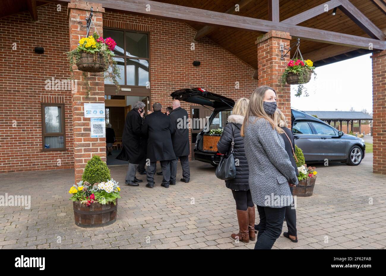 Inglaterra, Reino Unido. 2021. Portadores de pallos y llores en una entrada de crematorio con el carro funerario antes del servicio funerario. Durante el bloqueo del Coronavirus. Foto de stock