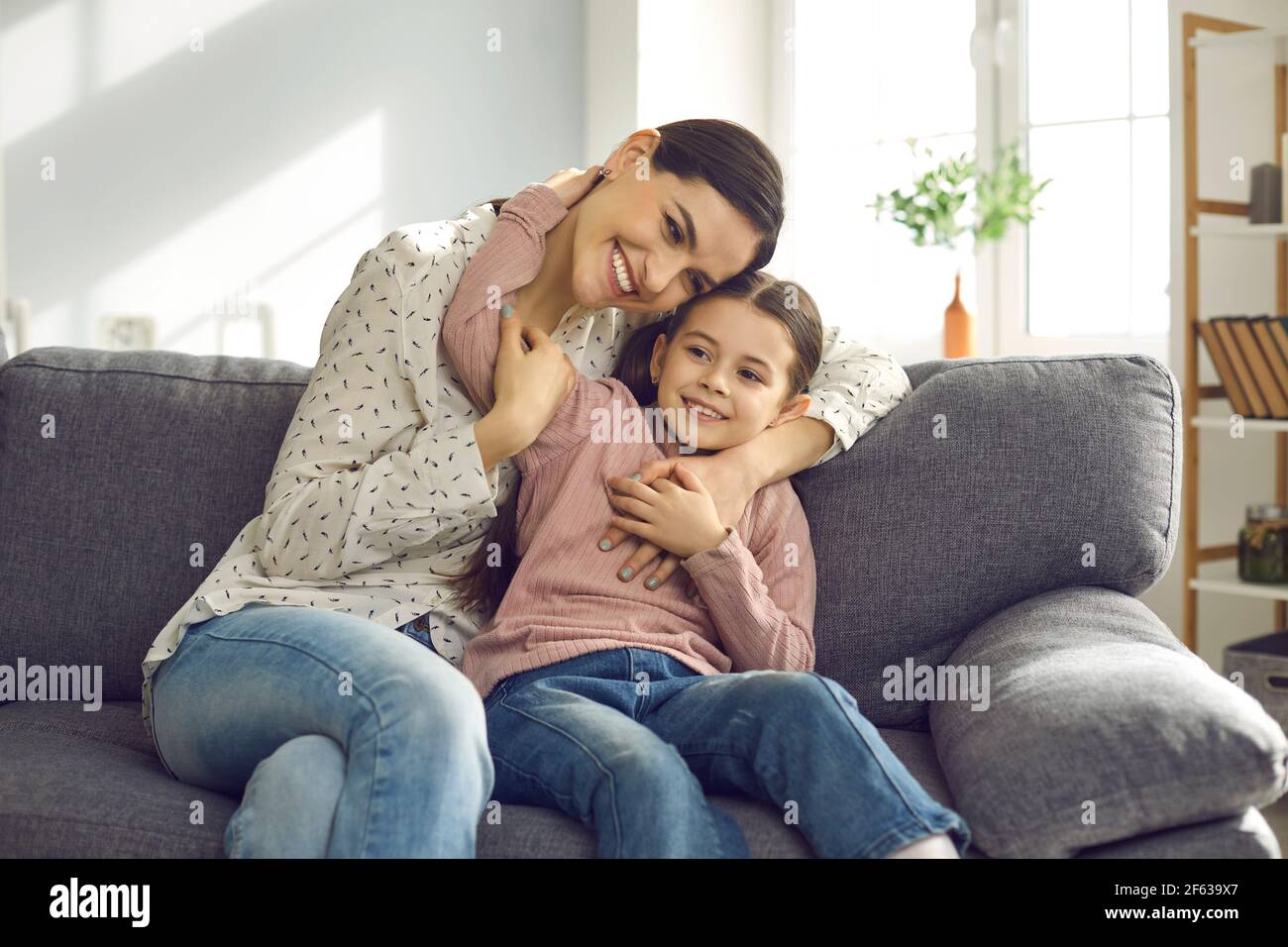 Retrato de feliz y sonriente joven madre abrazar con la hija sentarse en el sofá Foto de stock