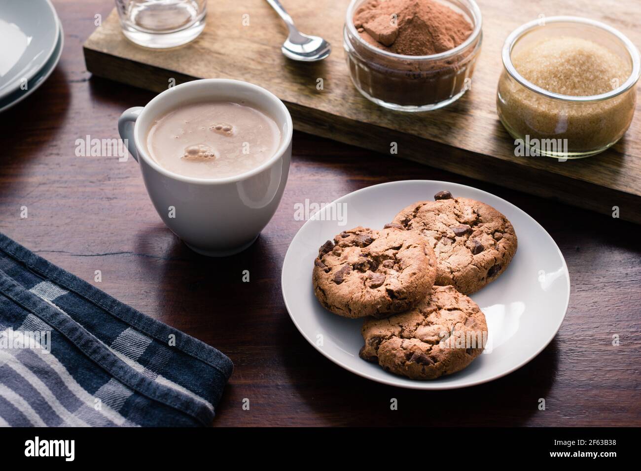 Galletas en un plato junto a una taza de chocolate en un escritorio de madera Foto de stock