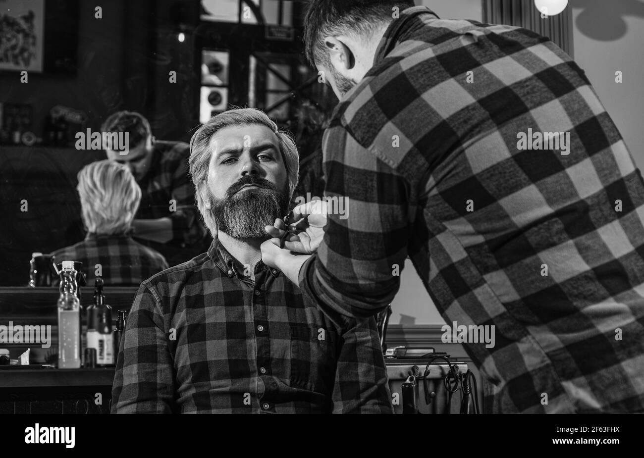 Retrato de masculinidad. Maestro barber hace el peinado y peinado con secador. Barbería. Joven hombre de cintura baja con barba cortando el pelo en un Foto de stock