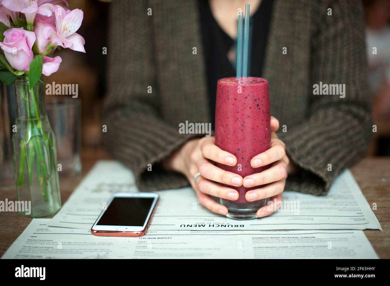 Manos femeninas sosteniendo batido de bayas rojas en el restaurante. Concepto de estilo de vida saludable. Londres, Reino Unido Foto de stock