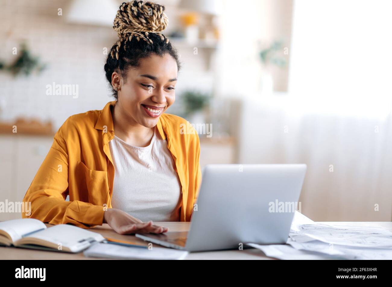 Inteligente atractivo feliz carrera mixta chica negra con dreadlocks, en ropa informal, estudiar a distancia, ver información en línea, hablar en conferencia con el profesor o colegas, sonriendo Foto de stock