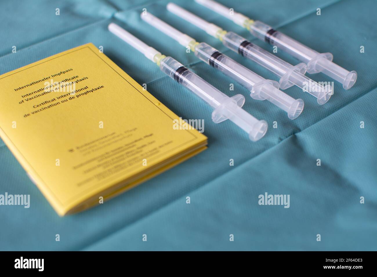 Concepto de vacuna con una serie de jeringas y amarillo internacional certificado de vacunación en tejido quirúrgico verde Foto de stock
