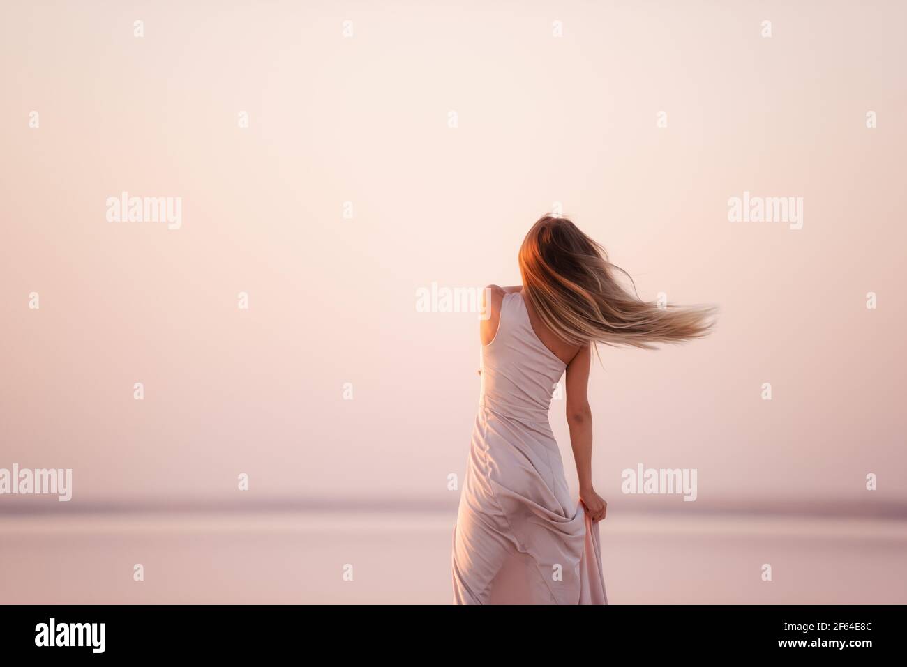 Retrato de una joven rubia en una noche de color rosa pastel, vestido en polvo sobre un fondo de hermosa puesta de sol. Chica con el natural de la creación, ha Foto de stock