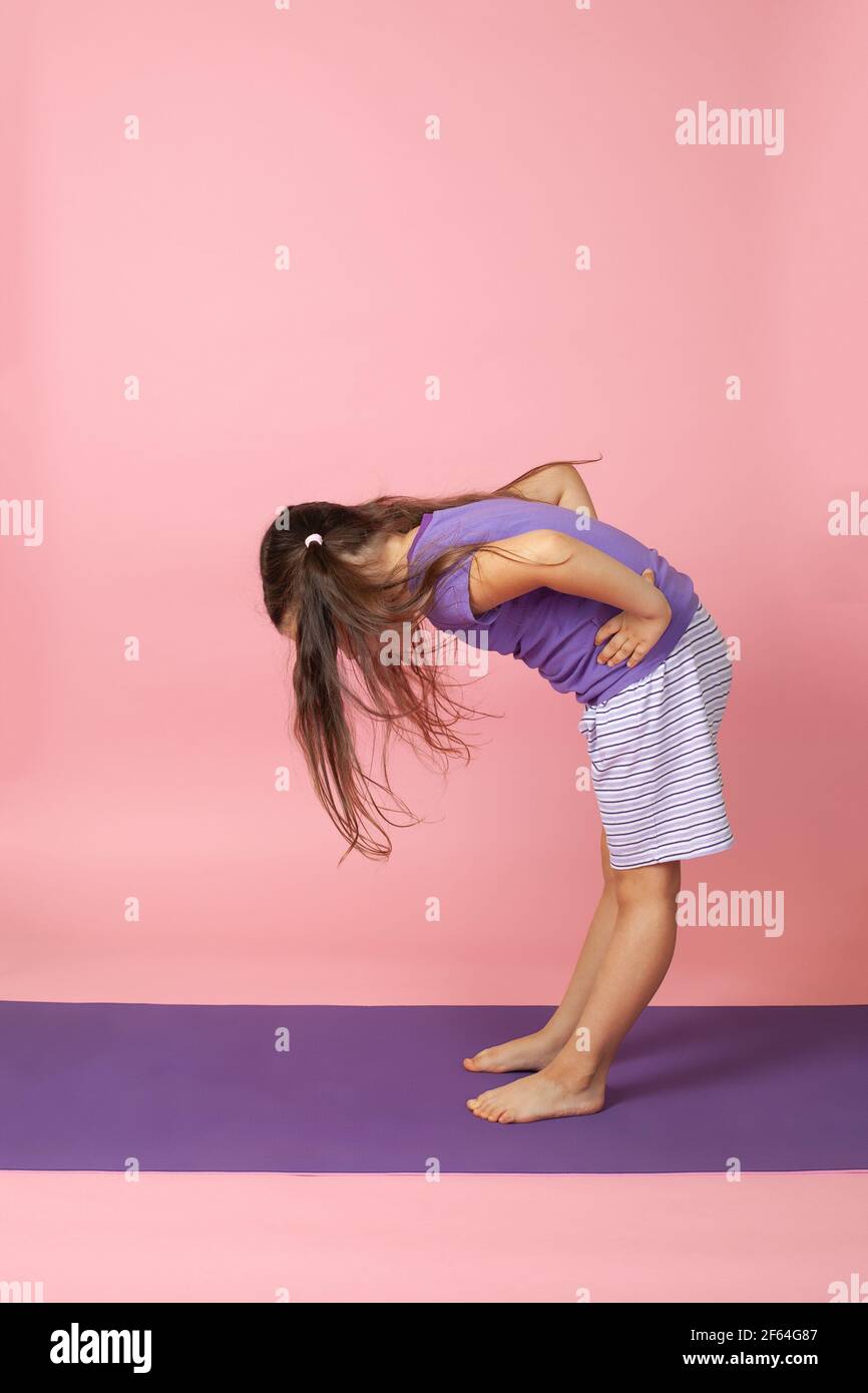 retrato completo de una chica con ponytails haciendo ejercicios matutinos y inclinándose hacia delante para la flexibilidad y la salud, aislado sobre un fondo rosa Foto de stock