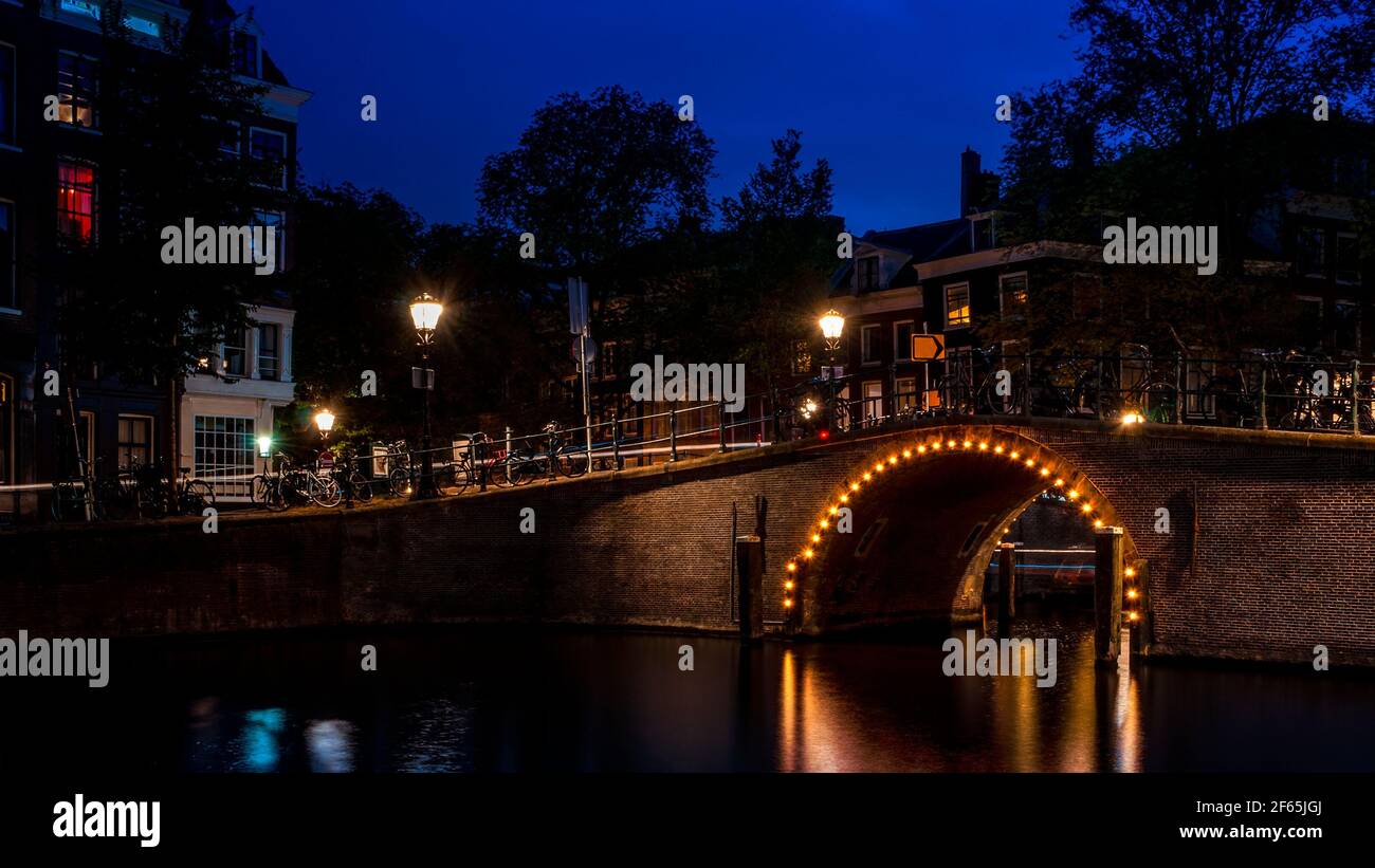 Puntos de referencia holandeses y destinos de viaje en el concepto Nederlands con Un puente sobre un canal en Amsterdam iluminado por la luz bombillas por la noche Foto de stock