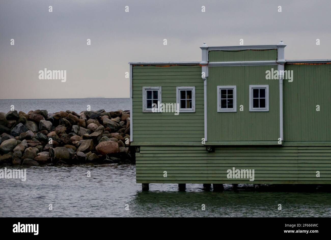 Una cabaña de madera verde se encuentra en el mar con una pared de rocas detrás de ella en Ribersborgsstranden, Malmo, Suecia. Foto de stock