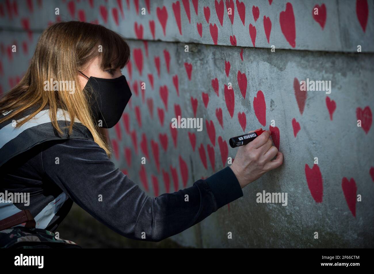 Londres, Reino Unido. 30th de marzo de 2021. Un voluntario dibuja corazones en una pared en Lambeth junto al río Támesis, y cada corazón representa a alguien que murió durante la actual pandemia del coronavirus en el Reino Unido. Llamado el Muro Conmemorativo Nacional de Covid, ha sido creado por las familias de duelo por la Justicia de Covid-19 y se extenderá por media milla cuando se complete. Crédito: Stephen Chung/Alamy Live News Foto de stock