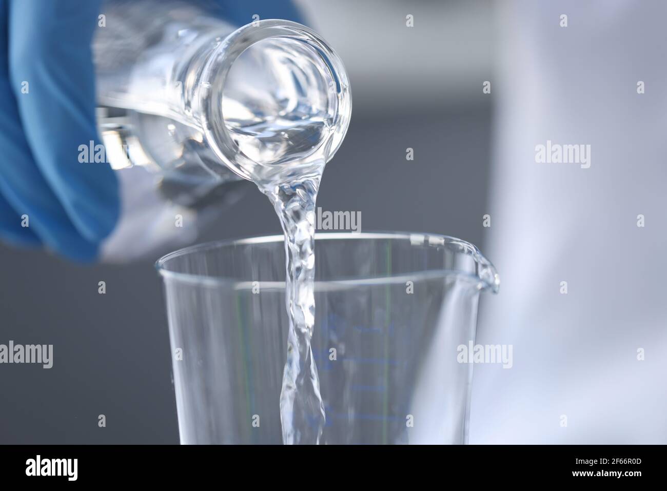 Químico científico en guantes vertiendo agua del frasco en el vidrio primer plano Foto de stock