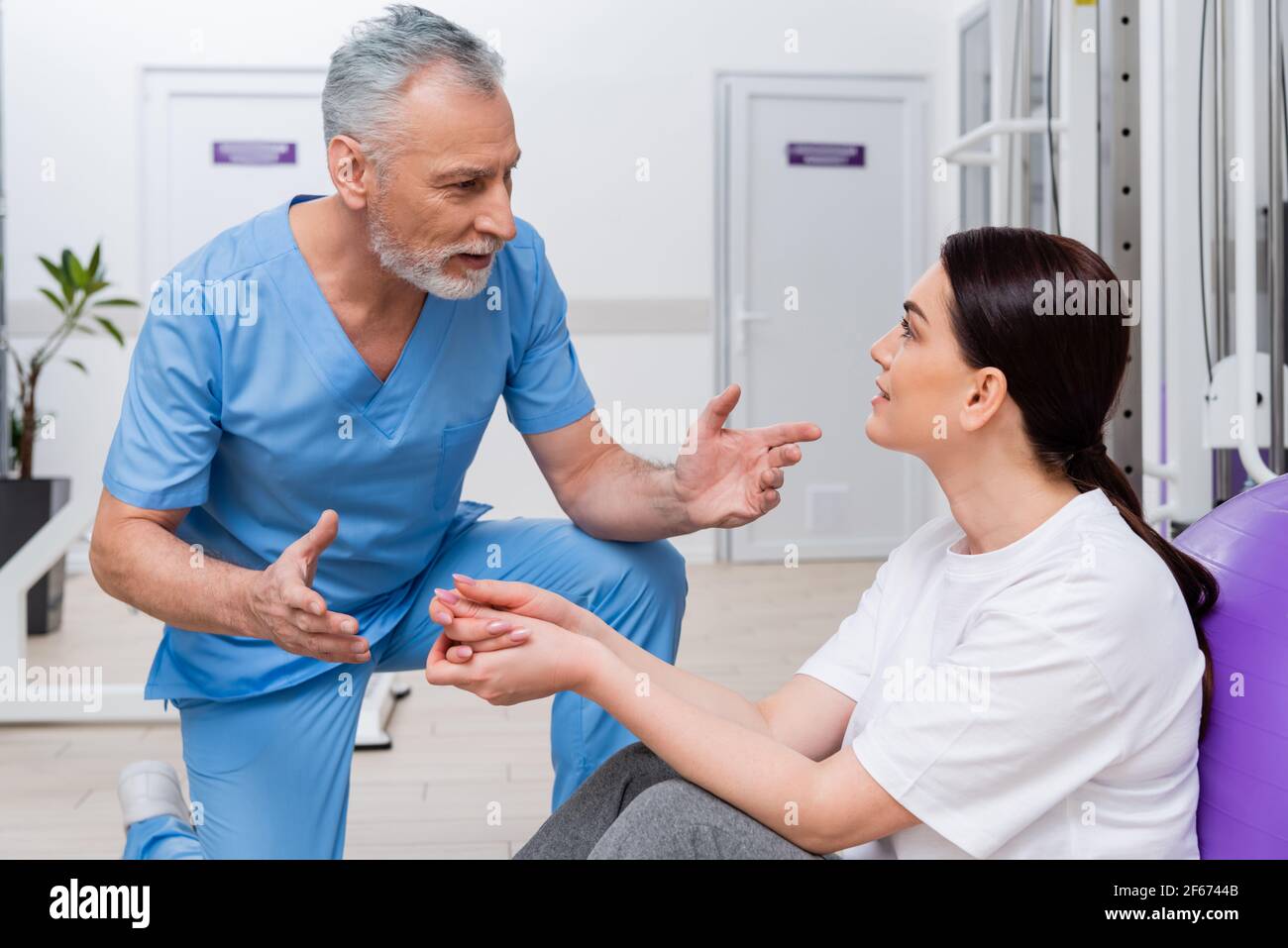 entrenador maduro gestuando mientras habla con la mujer en el centro de rehabilitación Foto de stock