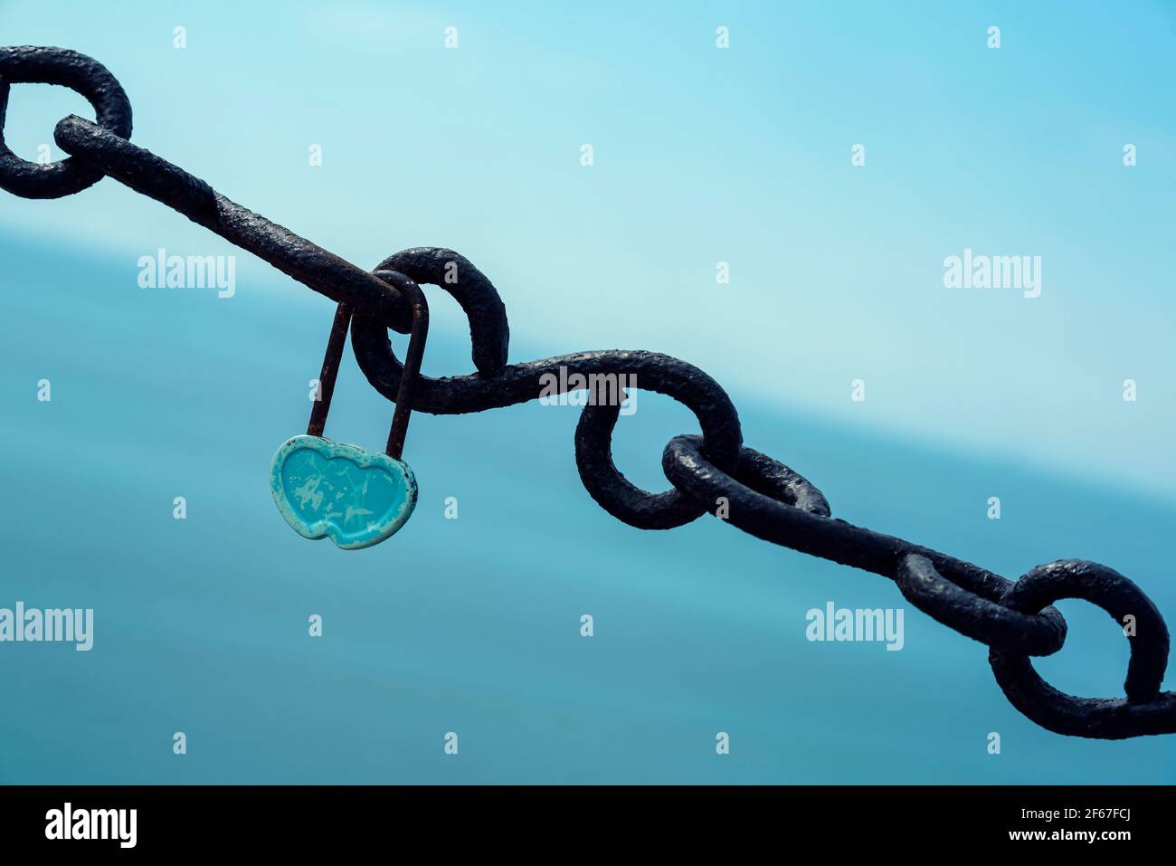 Candado azul con forma de corazón en una cadena negra en un Fondo azul símbolo de amor y fidelidad imagen horizontal Foto de stock