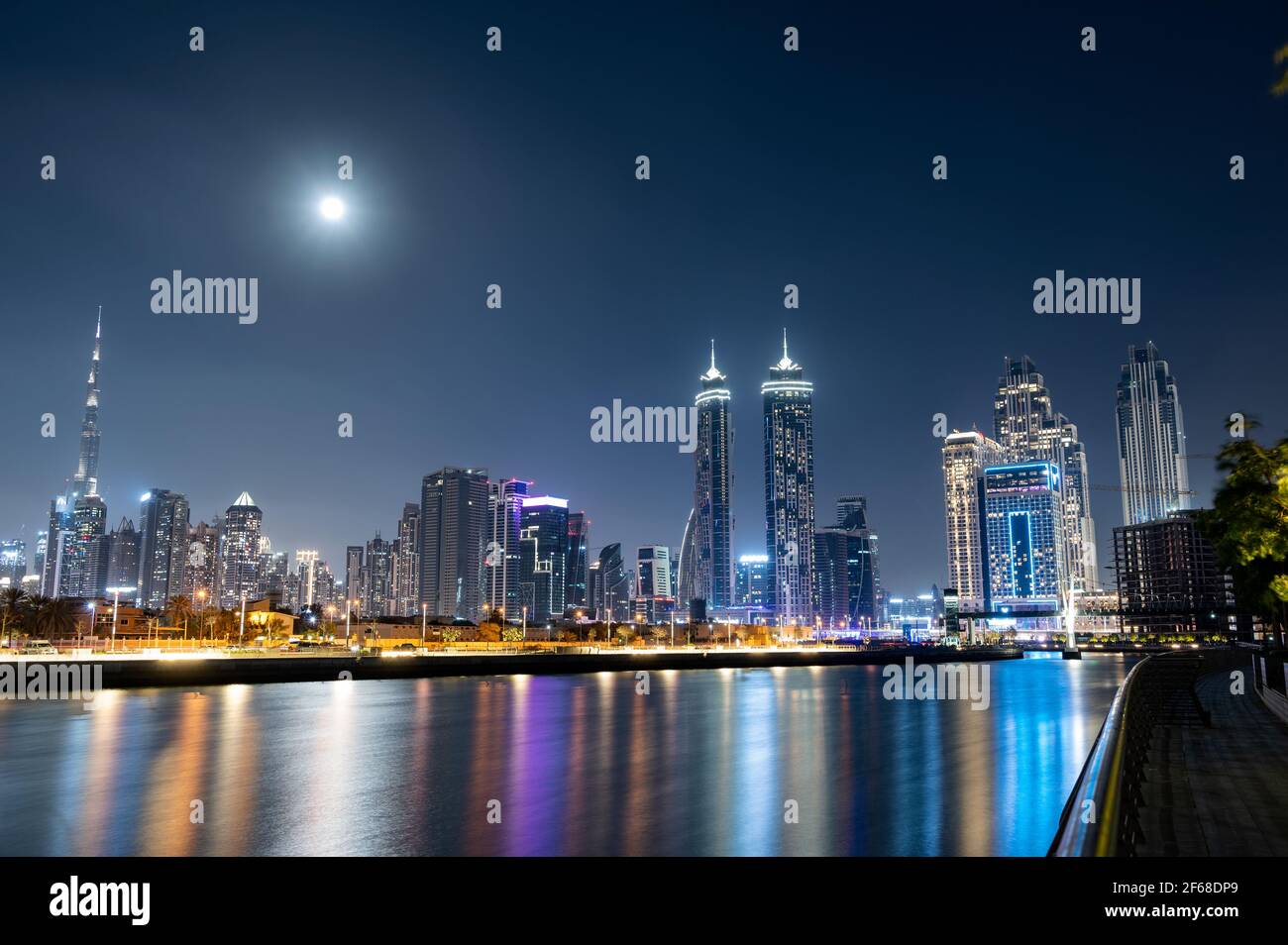 Vista panorámica del Burj Khalifa iluminado con otros skyscapers lanzando hermosas reflexiones sobre el agua capturada desde el paseo marítimo del canal de Dubai. Foto de stock