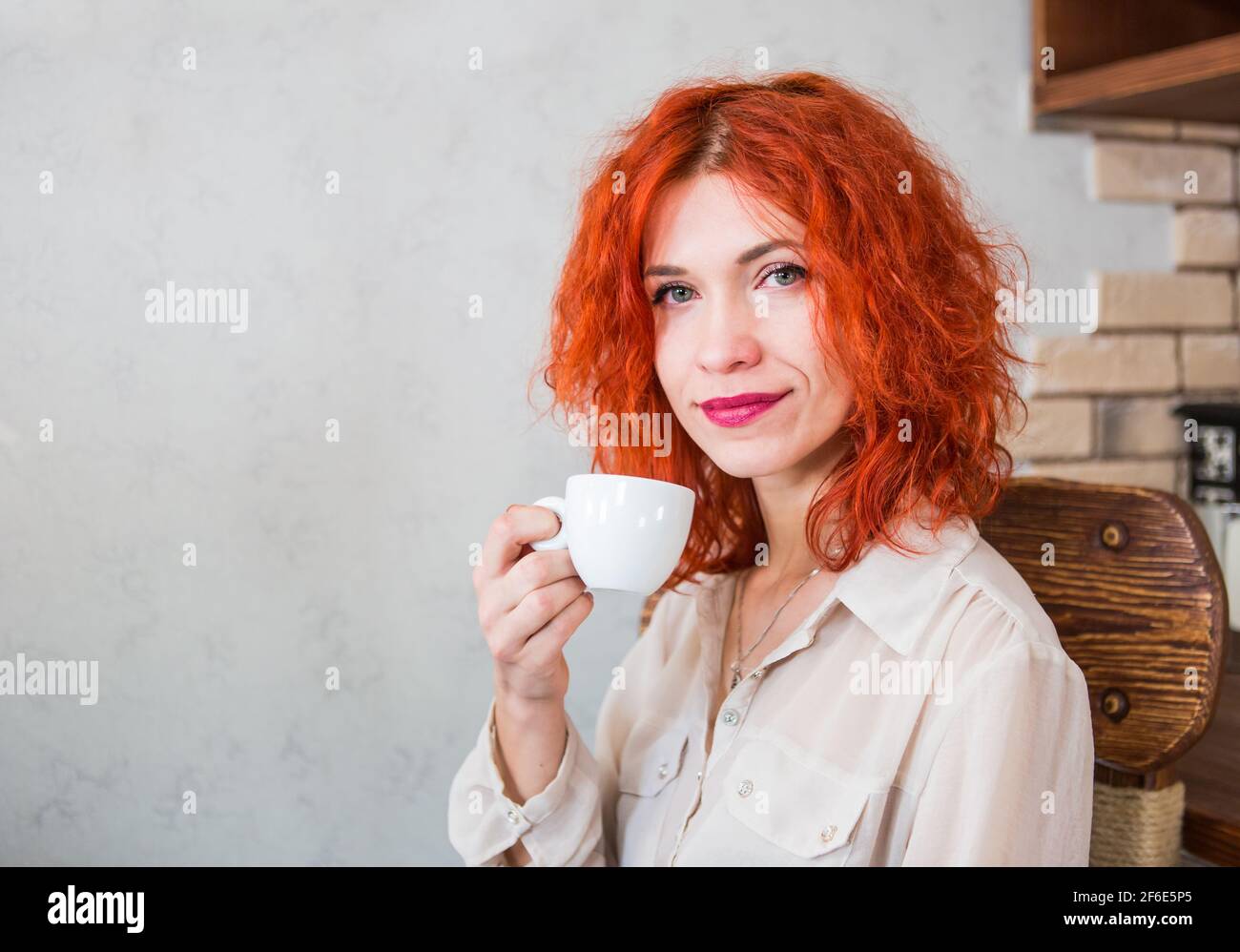 Hermosa niña con pelo rojo sentada en la cocina con una taza de café  expreso. Espacio para inscripciones, tema del café Fotografía de stock -  Alamy
