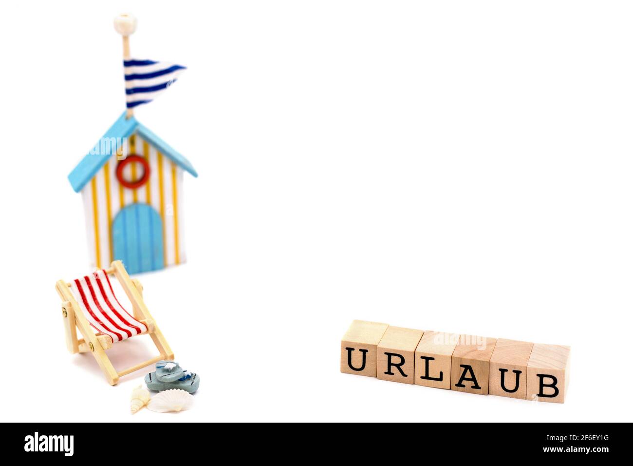 Silla de playa con sandalias, conchas, casa de baños, bloques de madera con texto vacaciones en alemán Foto de stock