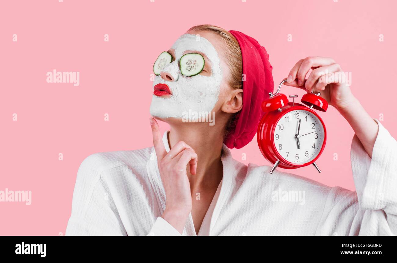 Mujer con máscara facial en la cara y reloj despertador en la mano. Mascarilla cosmética femenina. Tratamiento de belleza. Terapia de spa. Relájese. Foto de stock