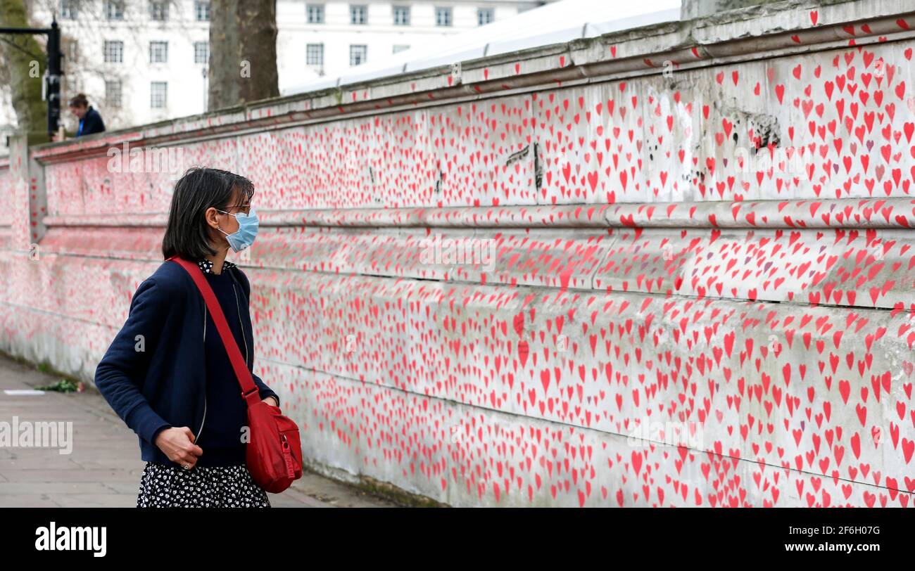 Londres, Gran Bretaña. 31st de marzo de 2021. Una mujer observa el muro conmemorativo del COVID Nacional en Londres, Gran Bretaña, el 31 de marzo de 2021. Los familiares y voluntarios que han sido afligidos están pintando corazones a lo largo de una pared de media milla frente a las Casas del Parlamento en Londres en recuerdo de los que murieron de COVID-19. Otras 4.052 personas en Gran Bretaña resultaron positivas para COVID-19, con lo que el número total de casos de coronavirus en el país asciende a 4.345.788, según cifras oficiales publicadas el miércoles. Crédito: Han Yan/Xinhua/Alamy Live News Foto de stock