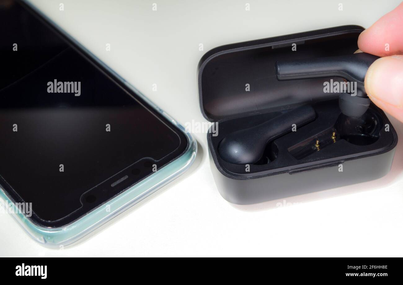 Primer plano PDV tiro de los dedos poniendo un par de modernos, batería operado, auriculares inalámbricos / auriculares en su estuche de carga, junto a un teléfono móvil. Foto de stock