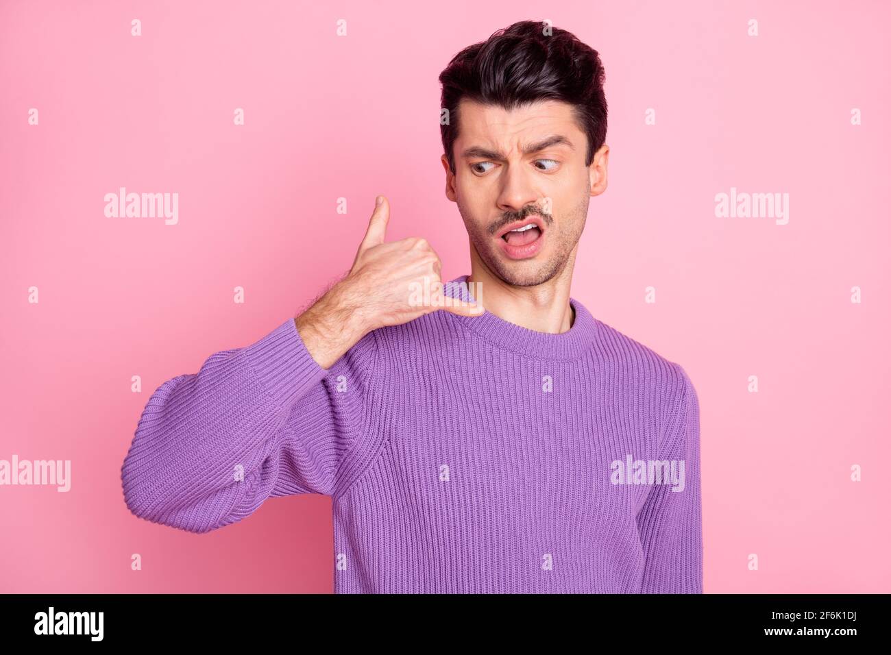 Retrato de un chico arrogante irritado atractivo mostrando señal de teléfono como llamando aislado sobre fondo color pastel rosa Foto de stock