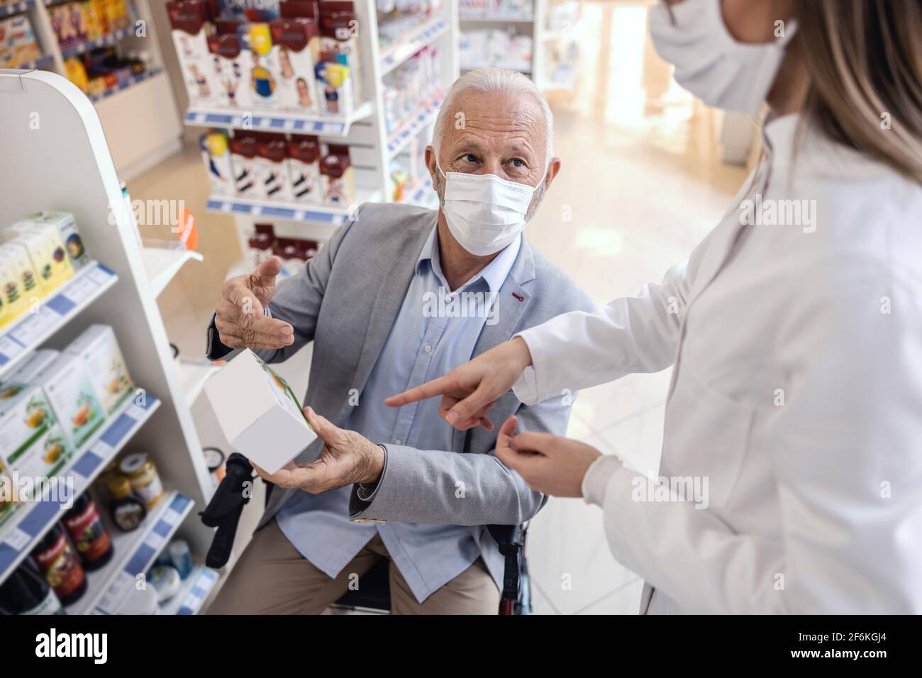 Un hombre en silla de ruedas habla con una farmacéutica en uniforme blanco  en la farmacia. Discusión sobre terapia médica y venta de drogas. Ambos  llevan un Fotografía de stock - Alamy