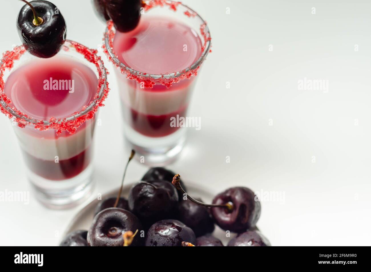 Cóctel de tres capas a base de vodka, licor de cereza y jarabe en vaso de  trago, decorado con cereza fresca y azúcar rojo, bebida de color Fotografía  de stock - Alamy