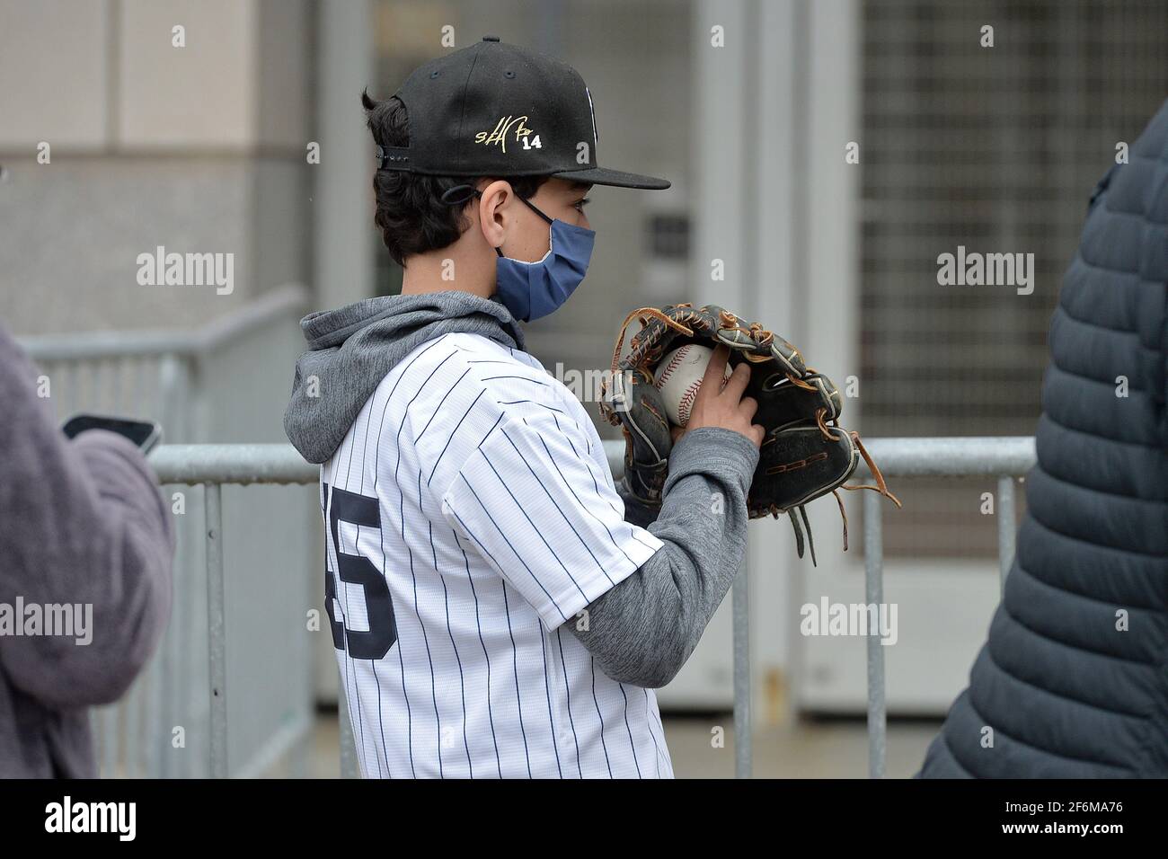 Un joven fan que lleva una camiseta de rayas y sostiene un guante de béisbol y una pelota espera en fila para asistir al partido de béisbol de los Yankees Nueva