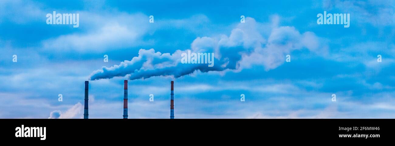 Contaminación ambiental, problema ambiental, humo de la chimenea de una planta industrial o central térmica contra un cielo azul nublado. Foto de stock