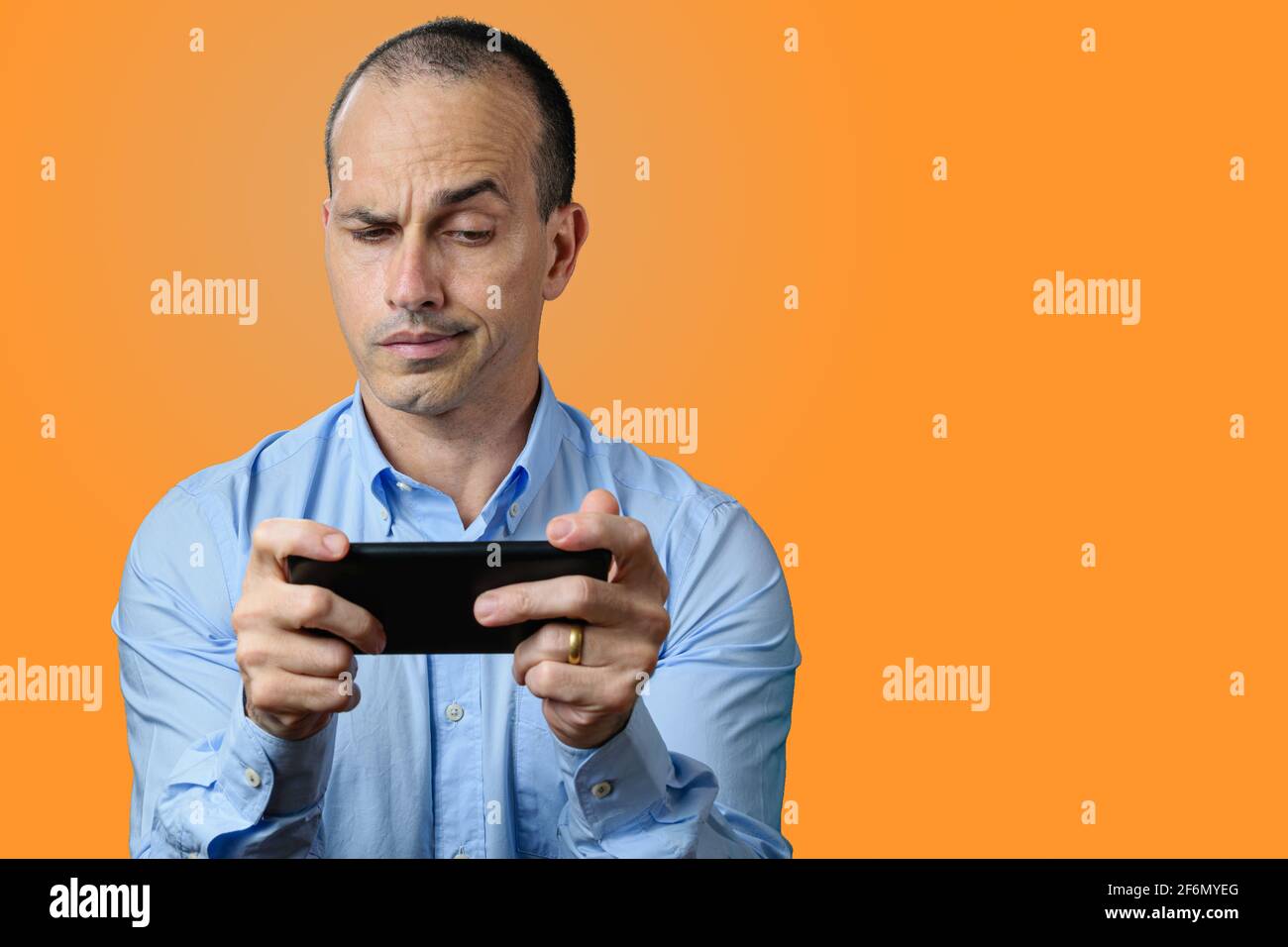 Hombre maduro con ropa formal, sospechoso y mirando a su smartphone. Fondo naranja. Foto de stock