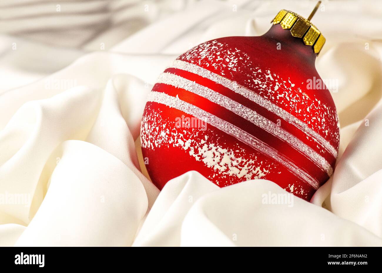 Tarjeta de felicitación de Navidad. Rojo brillante juguete de Navidad se  encuentra en un paño de seda blanca. Adornos navideños y un lazo de cinta  roja aislado en blanco. Colgando ba Fotografía