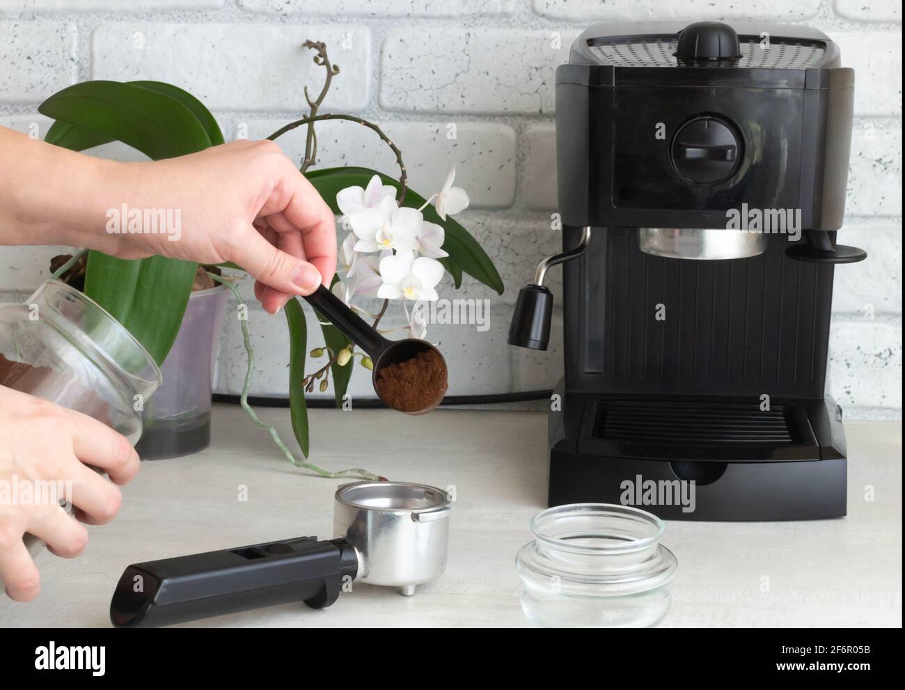 Una máquina de café negro está sobre la mesa de la cocina. Una mano vierte  el café molido en un cuerno. Concepto de elaboración de café casero.  Orientación horizontal Fotografía de stock -