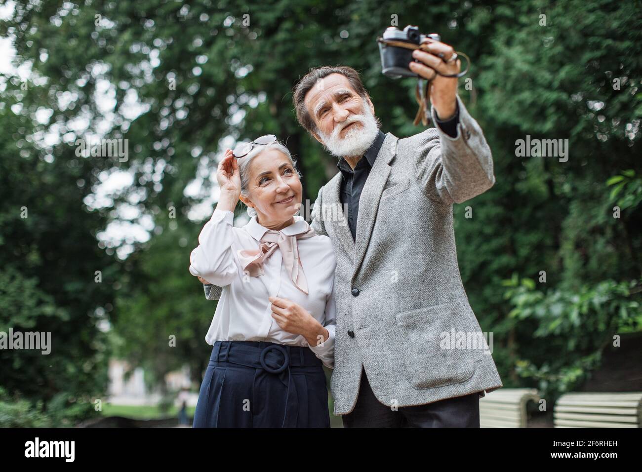 Hermosa familia mayor con ropa elegante que toma autorretrato en cámara retro. Feliz esposa y marido de pie en Green Park y disfrutar del tiempo soleado. Foto de stock
