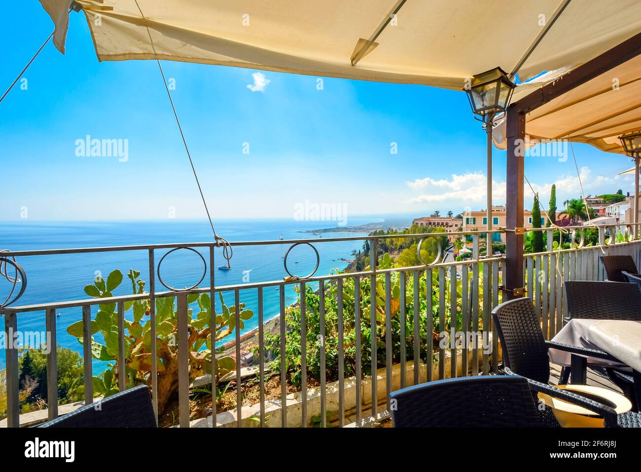 Vista desde el patio cubierto de un café en la ladera de una colina con asientos del mar Mediterráneo y la costa de Taormina, Italia, en la isla de Sicilia. Foto de stock