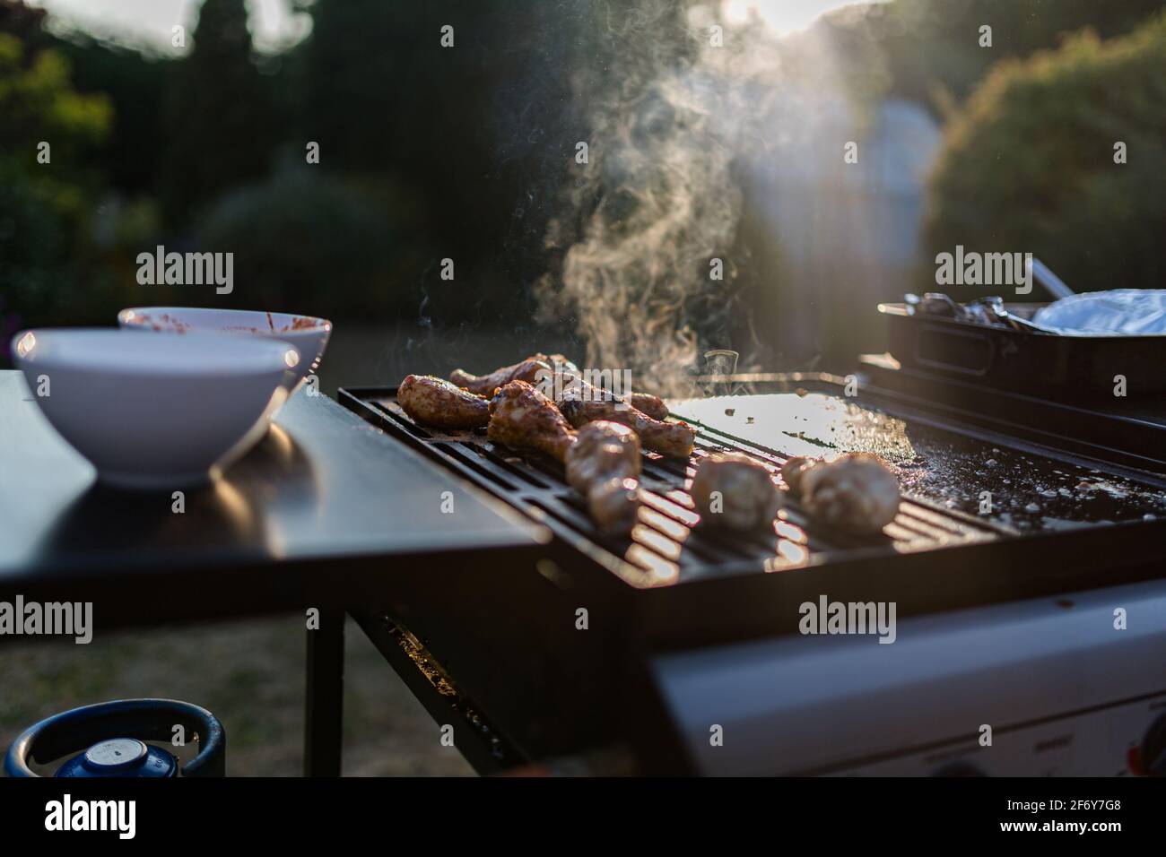 Cerca de una barbacoa con carnes cocinadas en ellos, el sol brillos en el fondo está atrapando el humo Foto de stock