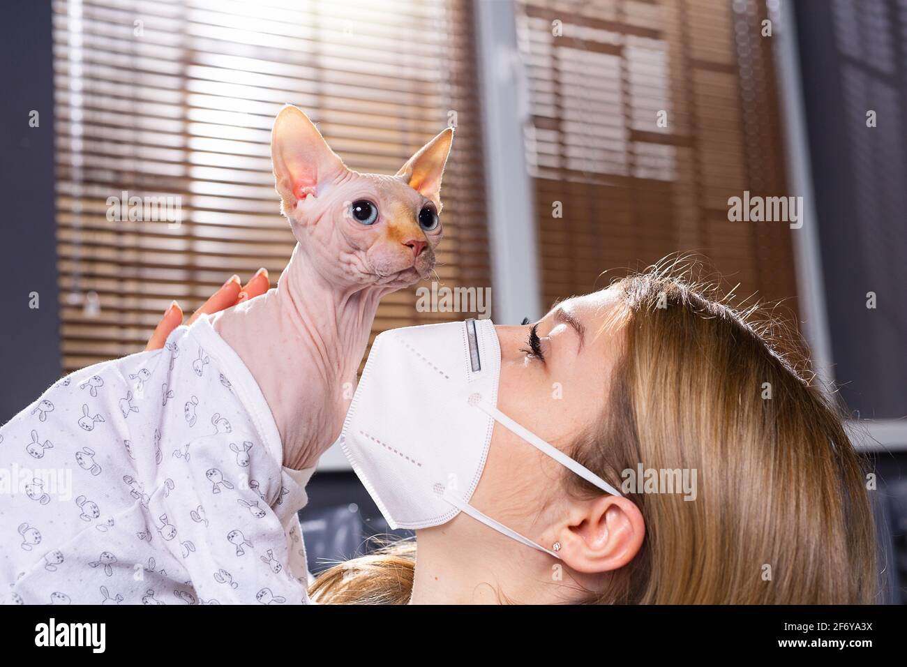 Mujer propietaria usando máscaras médicas para la protección del virus con  su gato encantador llevando ropa de moda, en casa, concepto de pandemia.  Sin besos gato Fotografía de stock - Alamy