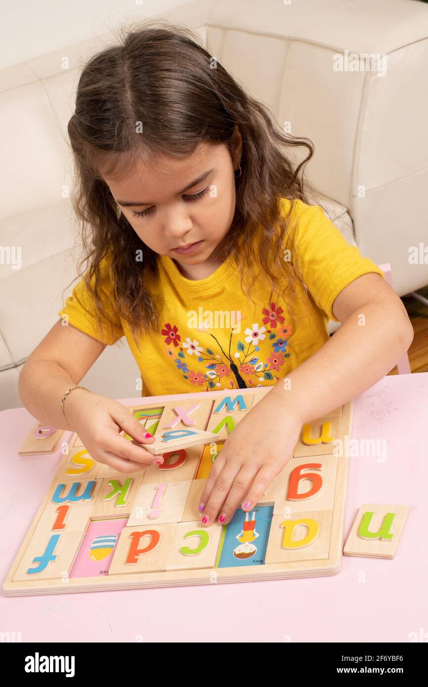 Niña de cuatro años jugando con un rompecabezas del alfabeto de madera, poniendo letras coloridas en sus manchas Foto de stock
