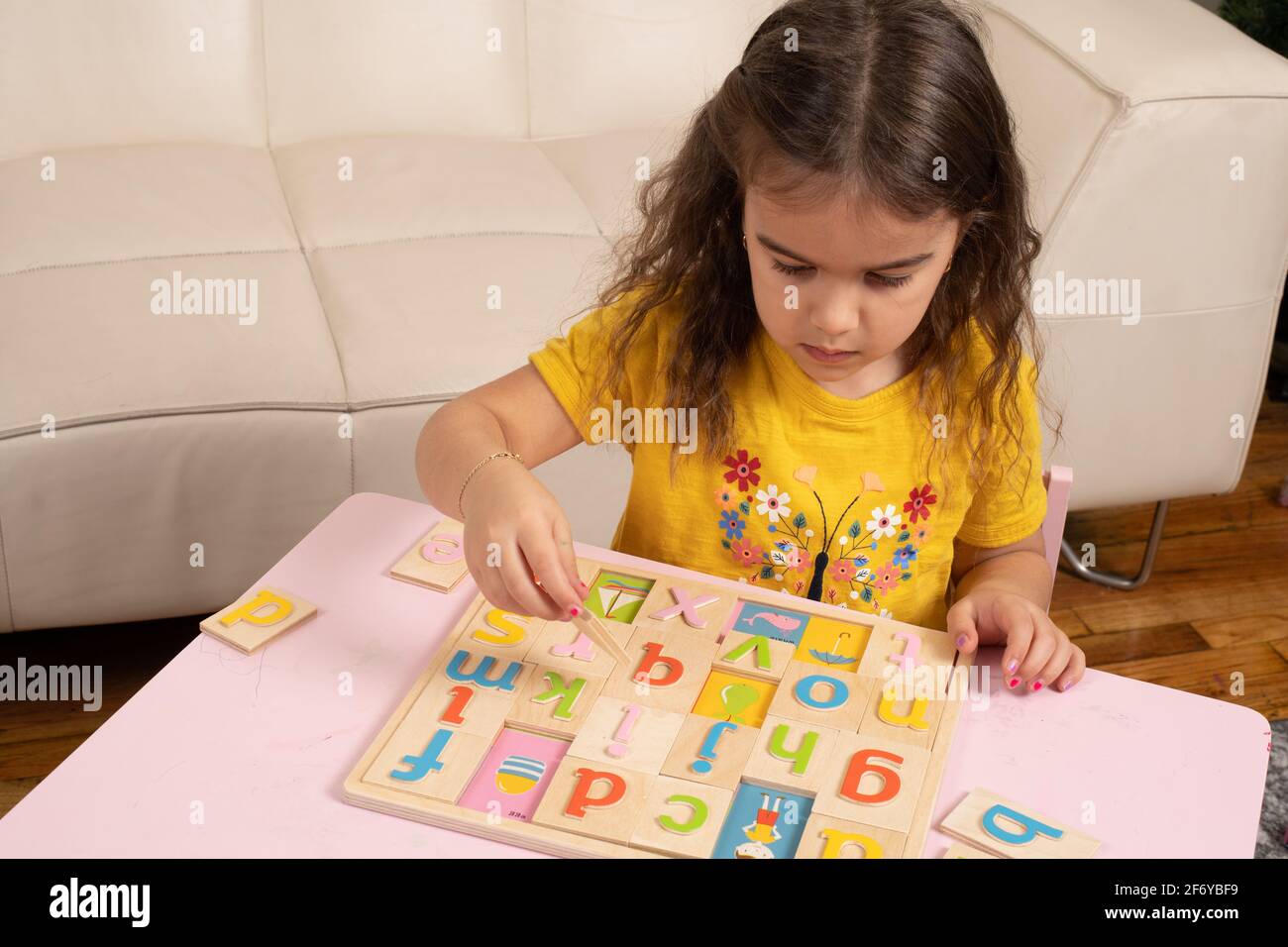 Niña de cuatro años jugando con un colorido rompecabezas del alfabeto de madera Foto de stock