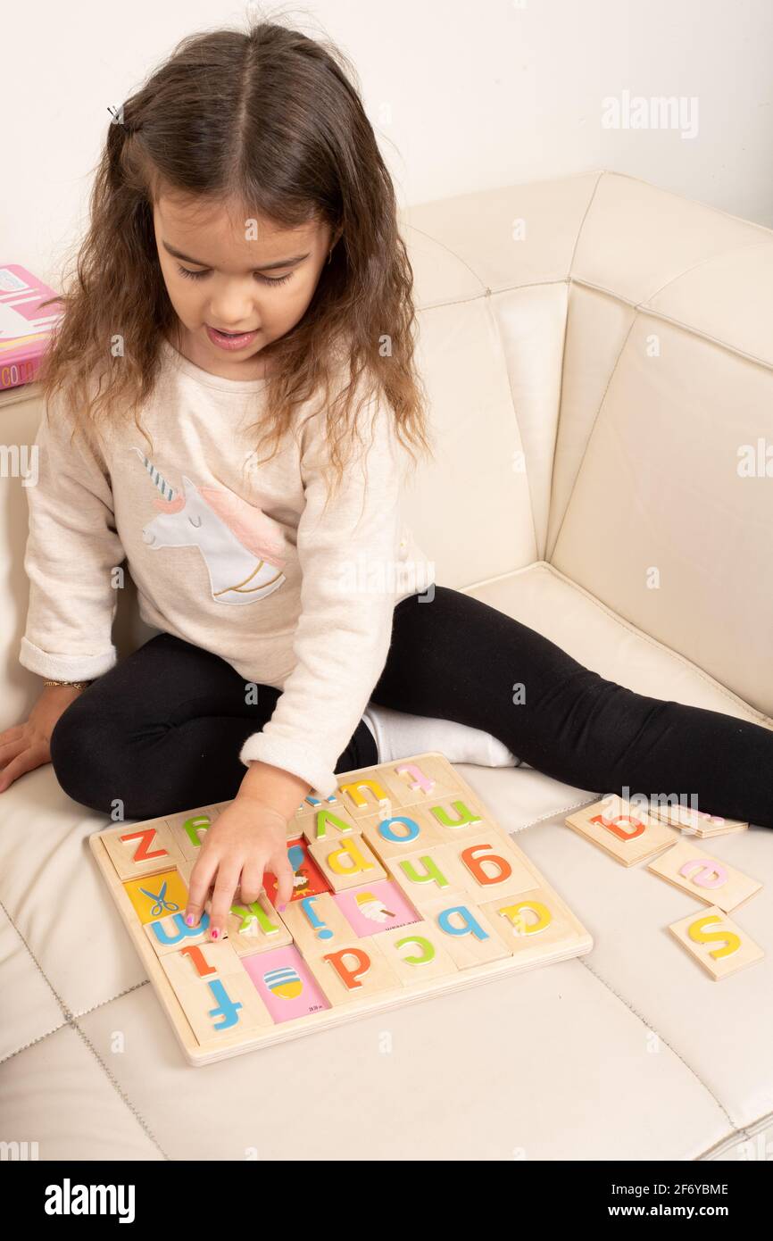 Niña de cuatro años jugando con el rompecabezas del alfabeto de madera Foto de stock