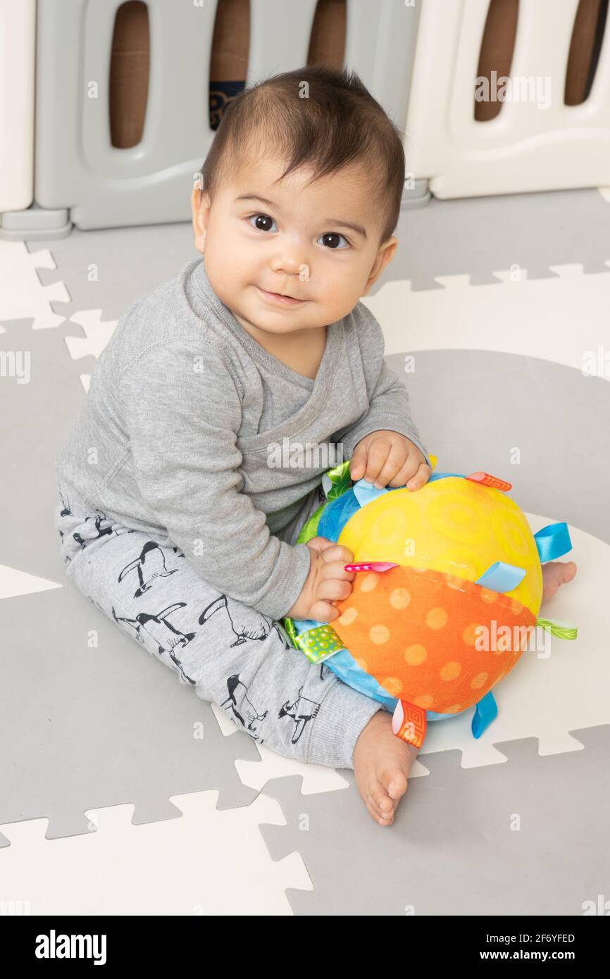 niño de 6 meses sentado retrato sosteniendo grande suave bola de juguete de tela Foto de stock