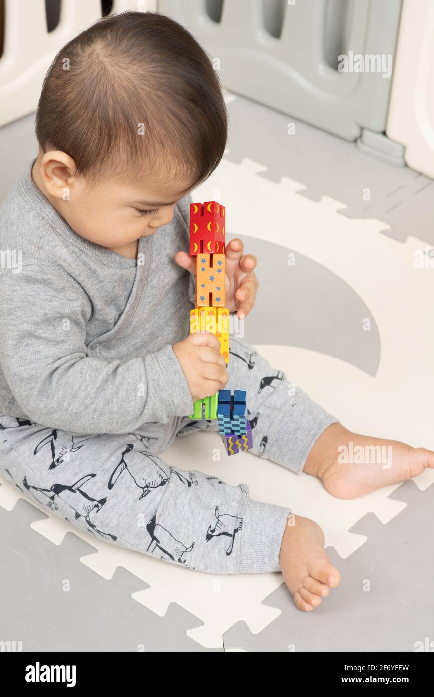 Niño de seis meses sentado, sosteniendo e inspeccionando el colorido juguete de madera, moviéndolo de una mano a la otra Foto de stock