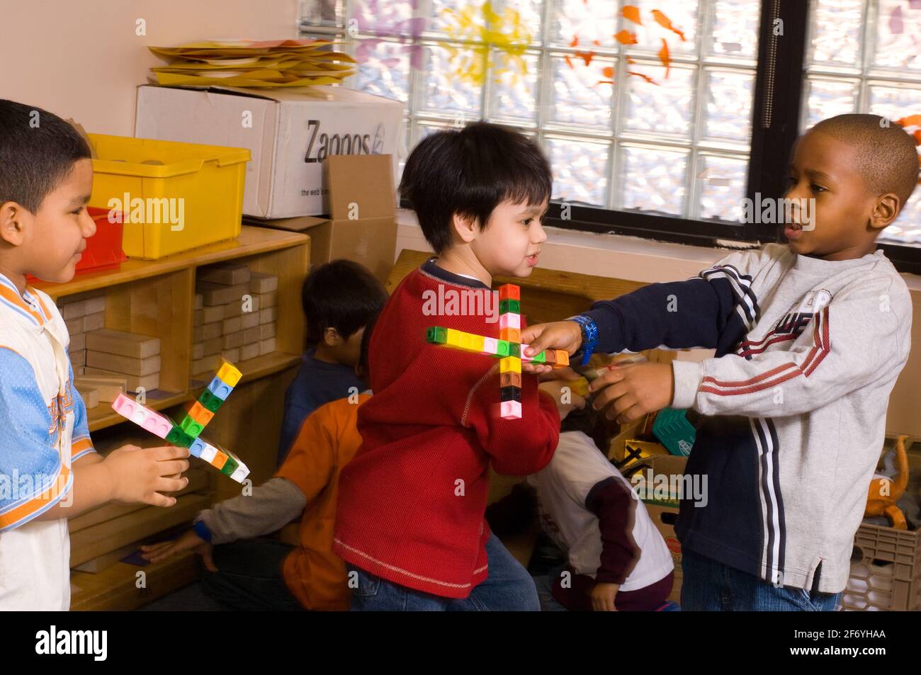 Educación preescolar grupo de tres niños jugando con armas hechas de cubos de conexión Foto de stock