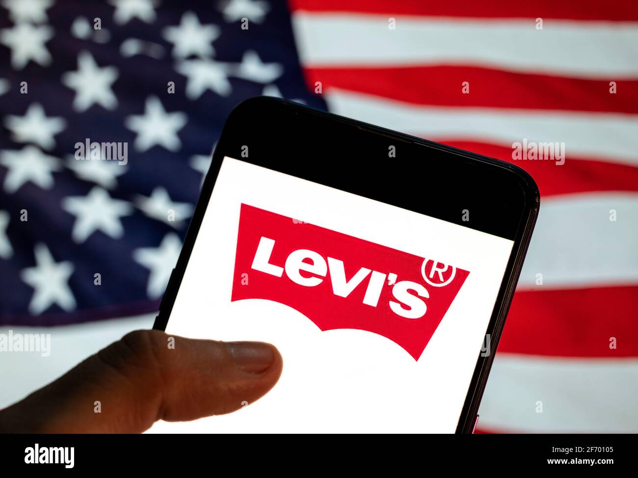 En esta ilustración de la foto el logotipo de la Marca de ropa americana  Levi visto en un smartphone con una bandera de los Estados Unidos en el  fondo Fotografía de stock -