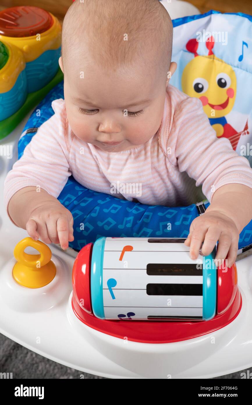 niña de 4 meses de edad en silla de bebé interesado en cilindro giratorio que hace un sonido cuando se mueve Foto de stock