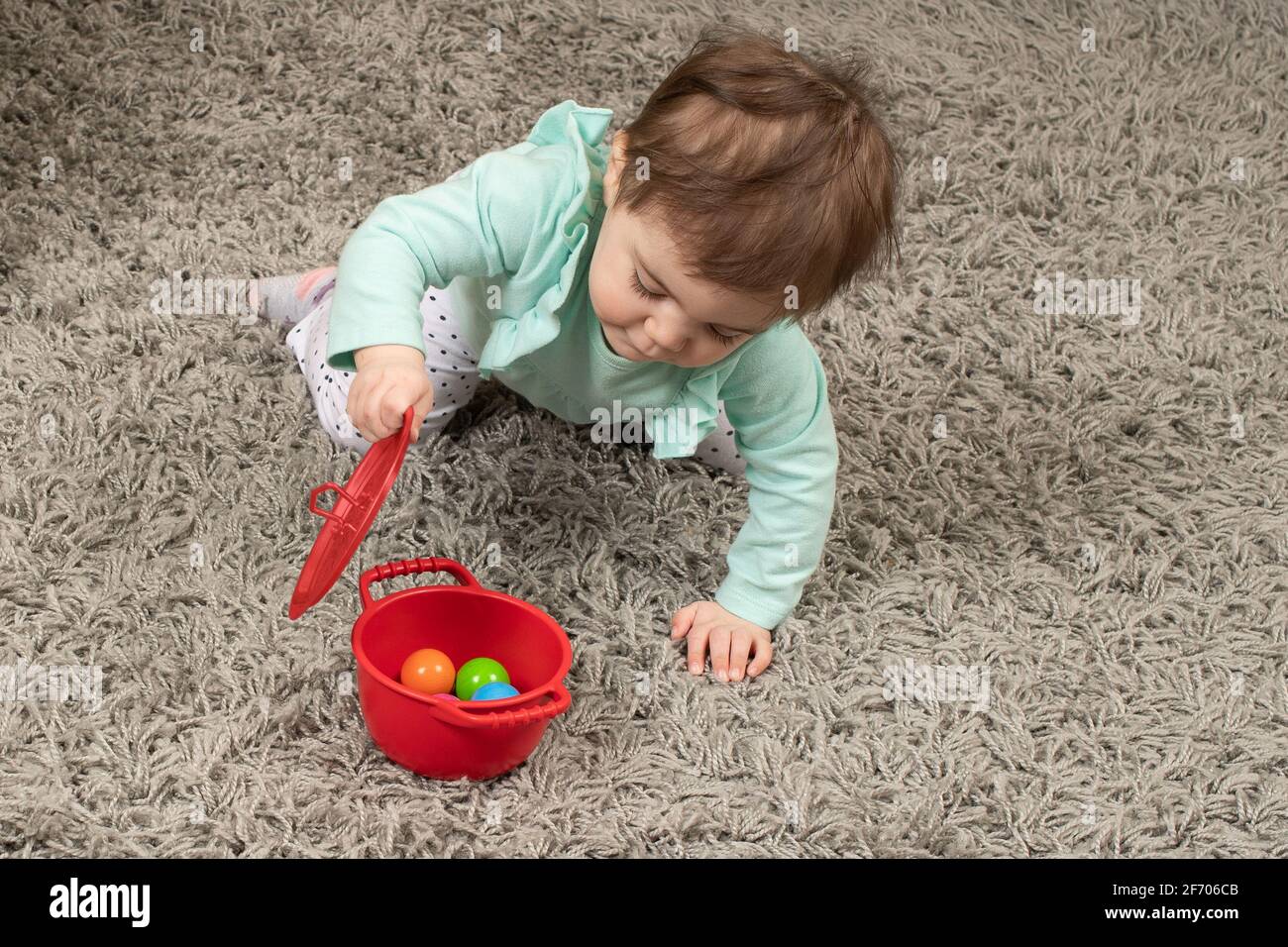10 meses de edad bebé niña abriendo la tapa en la olla Encontrar el juguete oculto Piaget objeto permanencia Foto de stock