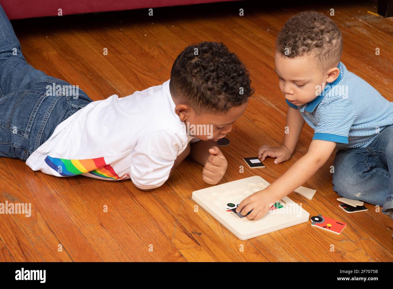 niño de 3 años haciendo rompecabezas de gancho, observado y ayudado por hermano de 7 años Foto de stock