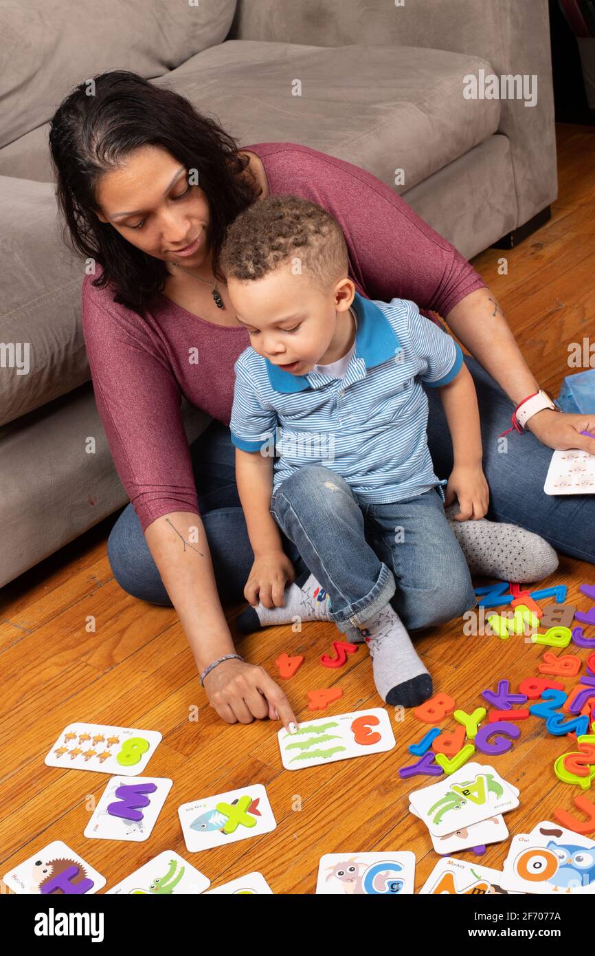 niño de 3 años con su madre, jugando con tarjetas de números que tienen una pieza de rompecabezas que cabe dentro de la tarjeta, contando y señalando el aprendizaje en casa Foto de stock