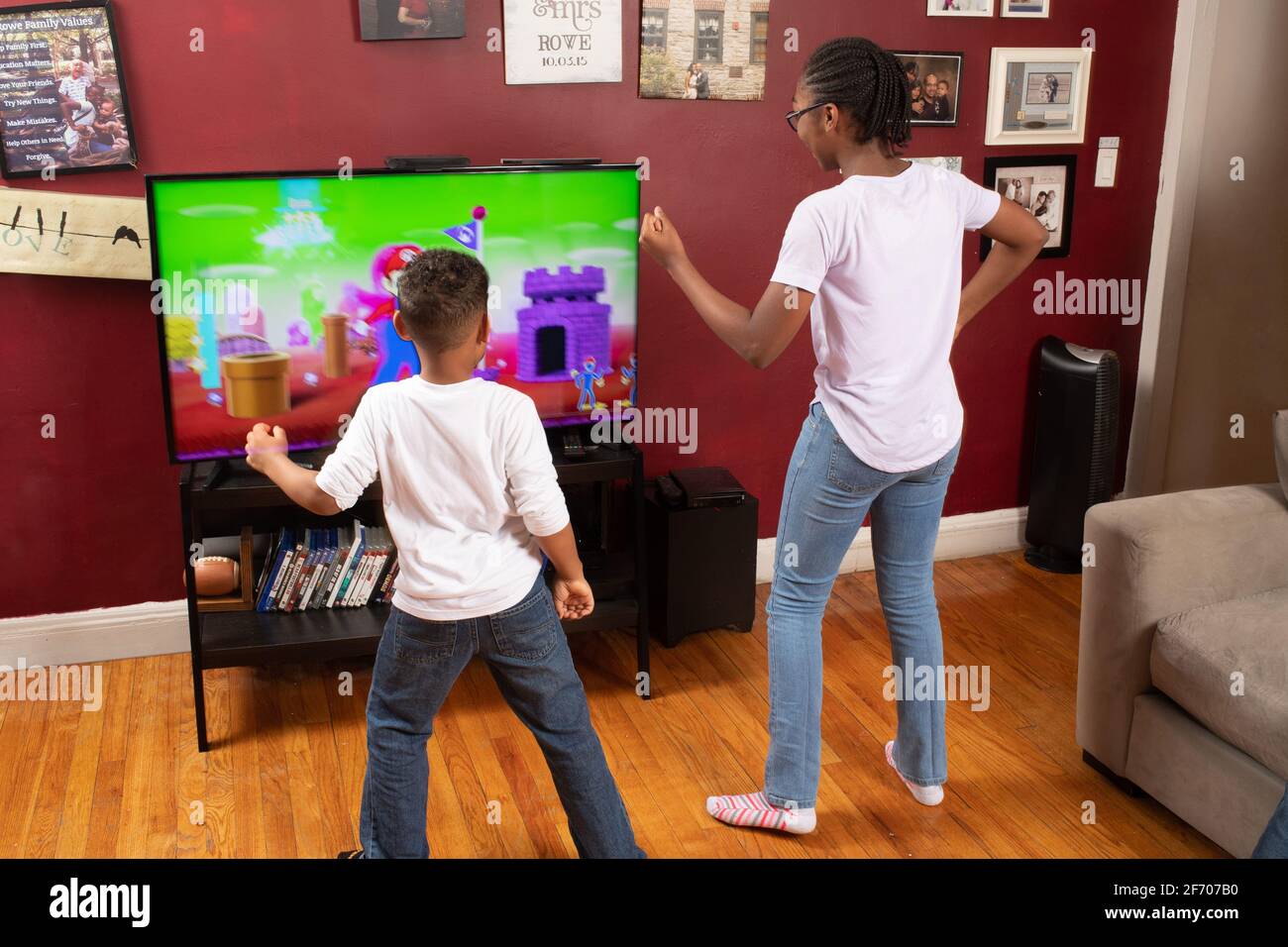 Dos niños de 7 y 12 años frente a la televisión pantalla haciendo ejercicio de baile de vídeo después de los movimientos de los personajes en pantalla mitad hermanos diversión en el interior Foto de stock