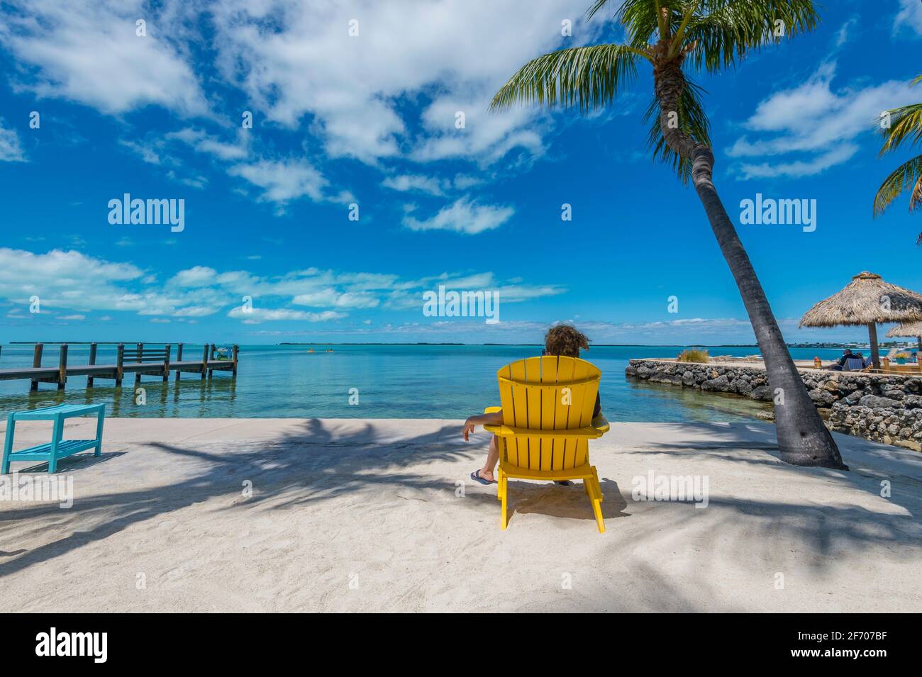 Mujer sentada en silla Adirondack amarilla, mirando contemplativamente al océano Caribe en un día soleado increíblemente hermoso. Foto de stock