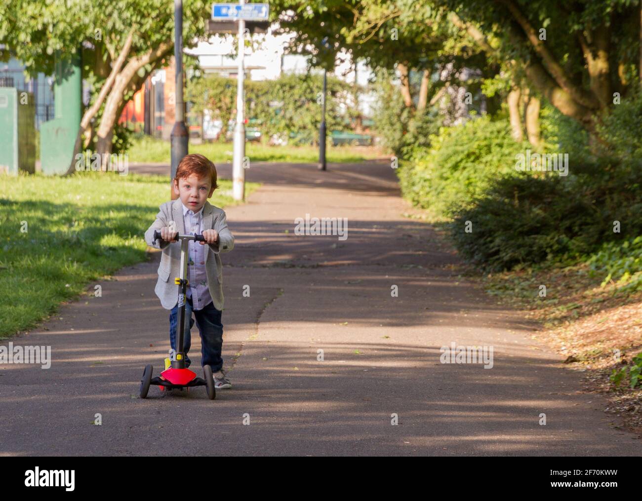 Lindo, Redhead Baby Boy montando una scooter en un parque Foto de stock